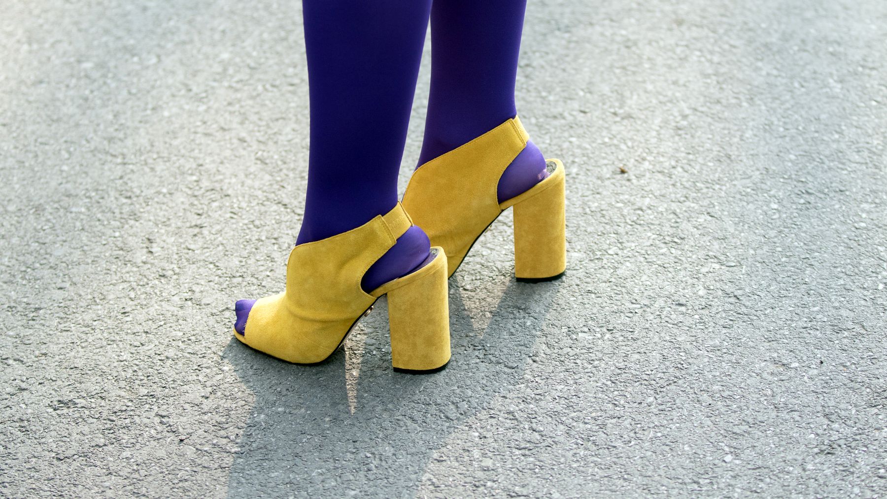 Dettaglio di stile: scarpe gialle e calze viola su asfalto